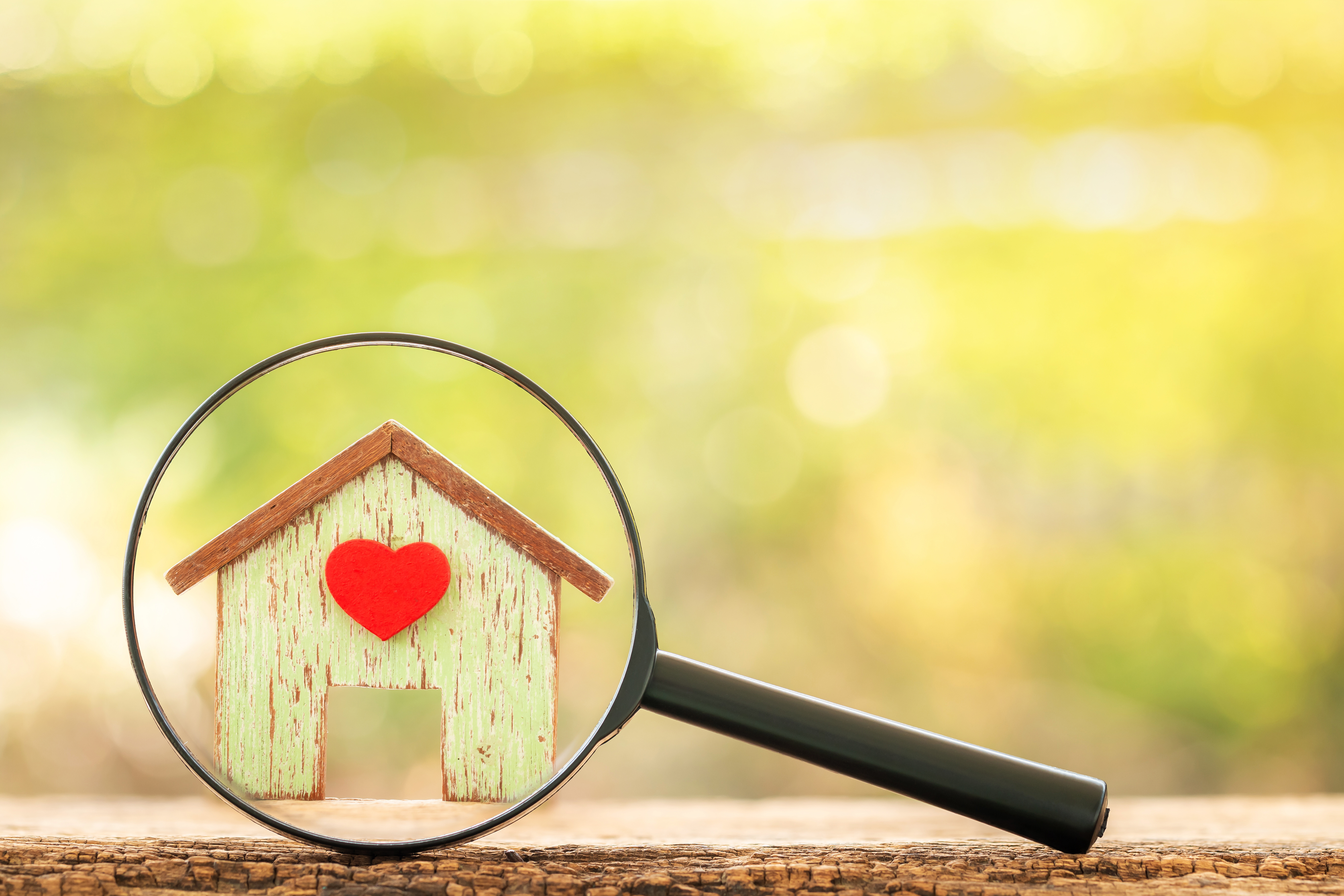 Magnifying glass with home model with red heart put on the wood